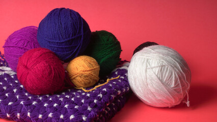 A Piece of knitting with color threads ball of yarn and a knitting needle on red background.