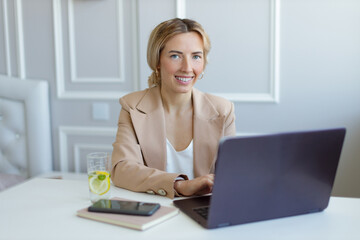 Portrait of a smilling business woman in a suit working on a laptop and drinking lemonade