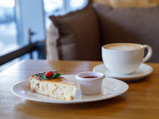Piece of cheese casserole or cheesecake, garnished with raspberry jam and cup cappuccino coffee on wooden table. Breakfast in cafe, top view, horizontal Traditional russian ukrainian breakfast