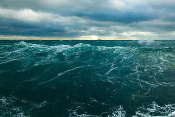 Heavy storm in the ocean. Big waves in the open sea, cloudy sky during a storm and a cargo ship on the horizon.	
