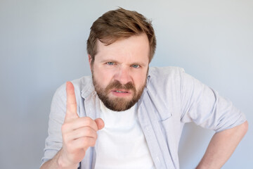 Irritated, disgruntled bearded man looks evil and threatening gesture with his finger. Gray...