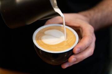 Latte heart poured by a barista closeup on hands