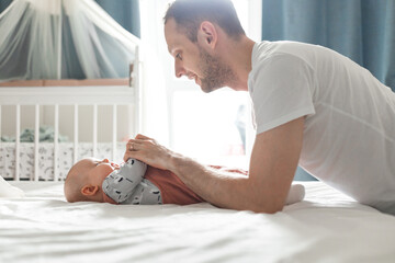 Side view of a young man playing with his little baby in bed
