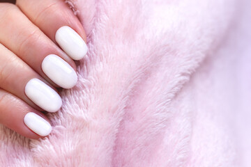 Female hand with beautiful manicure - white ivory nails on pale pink fluffy fabric, textile background with copy space