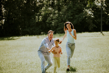 Happy young family with cute little daughter running in the park on a sunny day