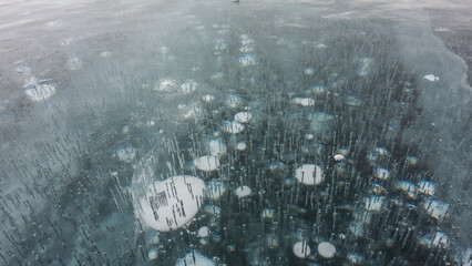 Transparent turquoise ice, close-up. Full screen. Cracks on the surface. Bubbles of frozen methane gas are visible in the depths. Baikal