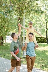 Fototapeta premium Happy gay couple walking with their daughter together in the park