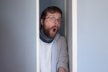 Bearded man in casual clothes is hiding in a closet, he peeps through the open door and looks in...