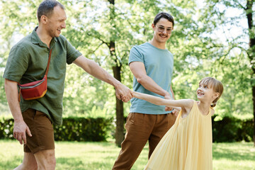 Happy gay family walking together with adopted daughter in the park in summer day