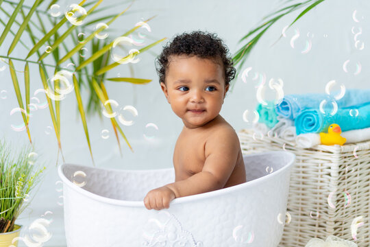 smiling African baby bathes and plays in the bubble bath at home, a concept of care and hygiene for young children