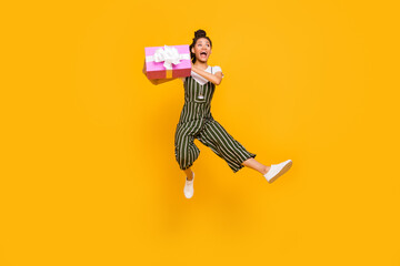 Full length photo of young afro girl happy positive smile jump up hold gift box party isolated over yellow color background