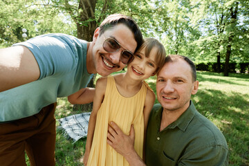 Portrait of happy gay male couple embracing with their adopted daughter and smiling at camera outdoors