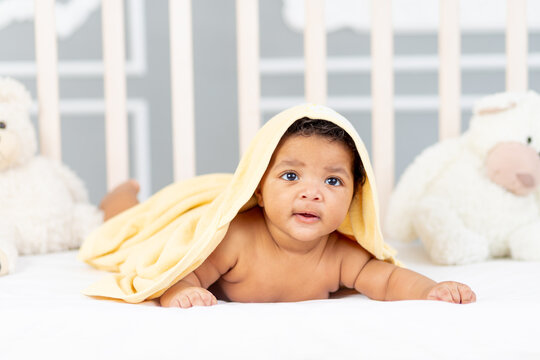 Smiling African-American little baby lies in bed after a bath in a yellow towel