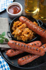 Close-up of bbq bratwurst sausages, sauerkraut and beer in the background, vertical shot, selective focus