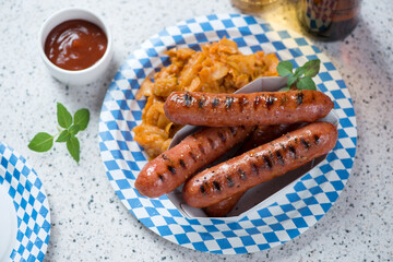 Blue and white carton plate with traditional german bratwurst and sauerkraut, elevated view on a beige granite background, studio shot