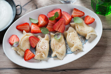 Curd dumplings or vareniki with strawberries served on a white oval plate, studio shot on a brown...