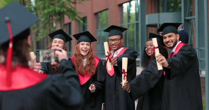Shooting. Young graduated people holding their graduation degree convocation ceremony and embracing while posing towards the camera with background of academy. Education concept