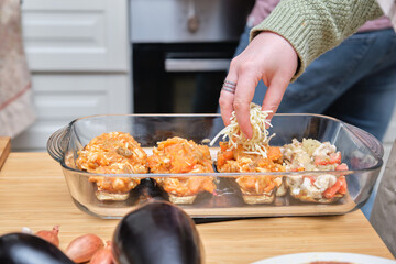 Unrecognizable young woman adding cheese to the stuffed aubergines. Cooking time.