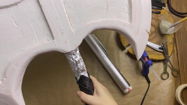 Celtic axe made of foamed polyethylene and with foil on handle in women's hands. Hatchet for festival or performance on wooden table. Cosplayer workshop. Handicrafts and diy.