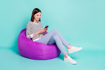 Photo of calm positive lady sit beanbag texting phone wear striped shirt isolated on teal color...
