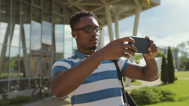 Tourist man taking picture with camera phone outside. Young African American man taking photo on phone on street.
