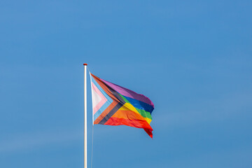 Worldwide LGBTQ community concept with progress pride flag (new design of rainbow flag) waving in the air with blue sky, Celebration of gay pride, The symbol of lesbian, gay, bisexual and transgender.