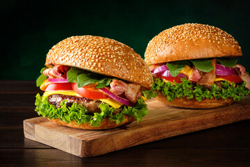 Two tasty burgers on a cutting board over green background. Fast food concept.