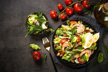 Seafood salad with green leaves, tomatoes shrimps, squid and octopus. Top view at black stone table.
