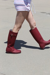 Red boots on a young lady walking along a swimming pool during early summer day