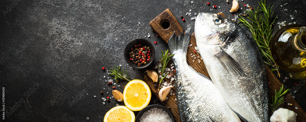 Wall mural Dorado, raw fish on black stone table with ingredients for cooking. Top view with copy space.