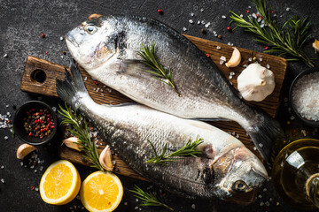 Fresh fish dorado on black stone table with ingredients for cooking. Top view.