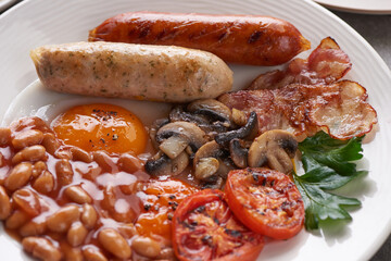 Traditional full English breakfast with fried eggs, sausages, beans, mushrooms, grilled tomatoes and bacon on a plate.