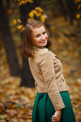 Autumn mood. Romantic happy Brown-haired woman in beige jacket and green dress smiles and walks in a park on background of beautiful autumn leaves. Fall coming. Autumn story. Yellow leaves in park