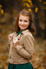 Autumn mood. Romantic happy Brown-haired woman in beige jacket and green dress smiles and walks in a park on background of beautiful autumn leaves. Fall coming. Autumn story. Yellow leaves in park