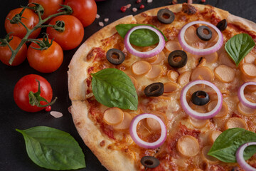 Italian pizza and pizza cooking ingredients on black concrete background. Tomatoes on vine, mozzarella, black olives, herbs and spices. Mixture pizza Italian food. Copy Space. Top view.