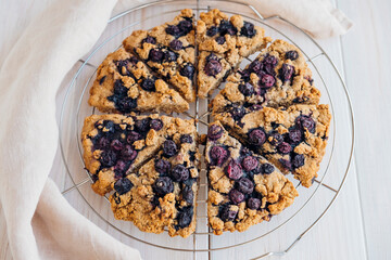 Freshly baked oat blueberry scones on cooling rack on white wooden background. Sweet food with natural ingredients. Vegan gluten free pastry..