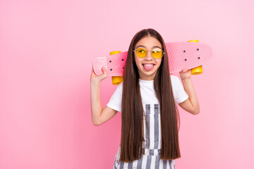Photo of cheerful funny small girl look empty space wear sunglass hold skate isolated on pink color background