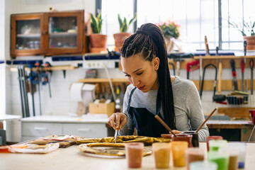 Young craftswoman coloring wooden detail in workshop 