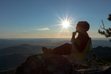 girl tourist meditating sitting on a rock against the backdrop of a sunset, a mountain valley and the sun with rays.  Travel camping and adventure lifestyle concept.