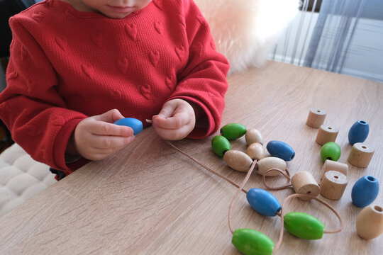 small child, toddler stringing colored wooden beads on a string, children's fingers close-up, concept of development of fine motor skills, tactile sensations, creativity, children's entertainment