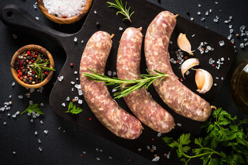 Bratwurst or sausages on cutting board with spices at black table. Top view.