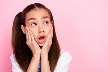 Photo of amazed shocked dreamy small girl look empty space hands cheeks isolated on pink color...
