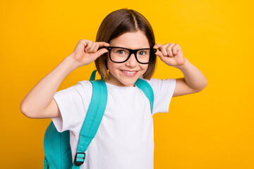 Photo portrait small schoolgirl smiling wearing glasses blue backpack isolated vivid yellow color...