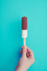 vanilla ice cream with chocolate on a stick held by a child's hand, with copy space against mint green background