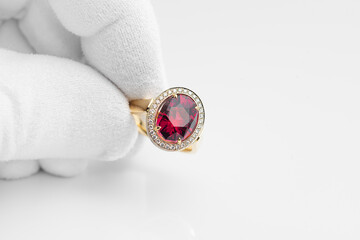 Golden ring with rhodolite gem and diamonds in jeweler hand in a white glove