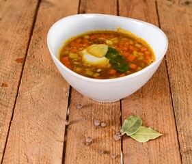 Red soup with carrot and ginger in white and green plate on wooden background.