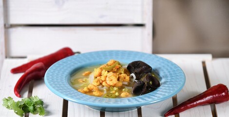 Green soup with prawns, chilli papper, coriander, jalapenio and pasta on blue  plate on wooden background.
