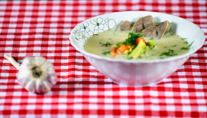 Green soup with meat, carrot, cream, garlic, broccoli and dill on a white plate on wooden background.