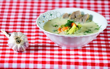 Green soup with meat, carrot, cream, garlic, broccoli and dill on a white plate on wooden background.