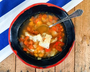 Red, fish soup with chilli papper, carrot, fish parsley and pore in a red and black bowl on wooden...